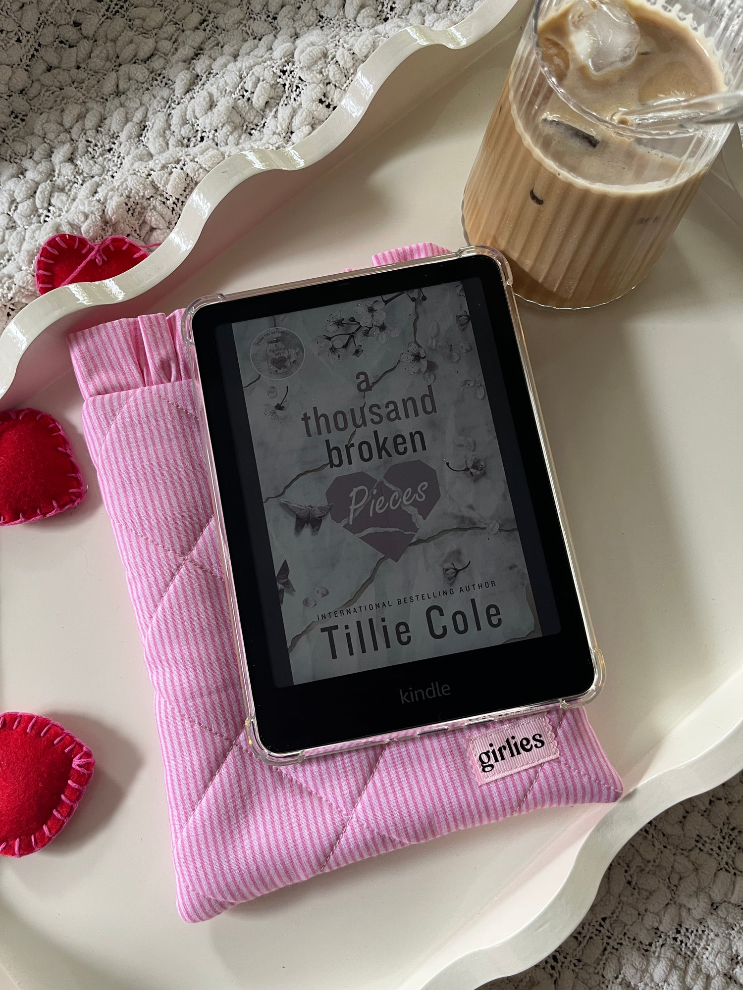 E-reader on a pink cushion with a book cover displayed, next to a glass of iced coffee.