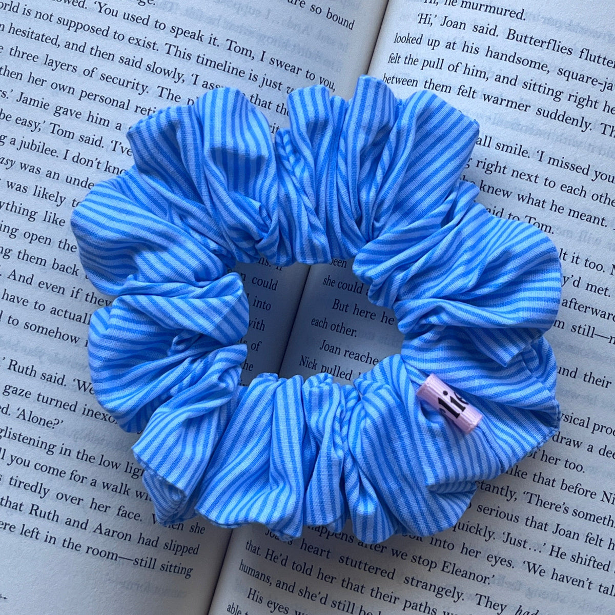 A blue knotted hair accessory with a small pink bow, displayed on the pages of an open book.