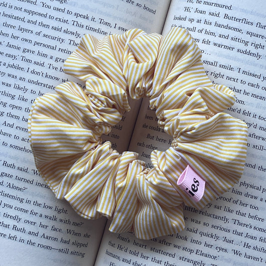 A striped fabric bookmark with yellow and white diagonal stripes and a pink tag reading 'JES', placed on an open book.